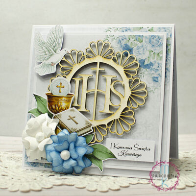 Kartka kwadratowa w środkowej części znajduje się ozdobna ramka z beermaty z napisem IHS. W górnym lewym rogu znajduje się gołąb, w prawym górnym rogu jest grafika niebieskich kwiatków. W lewym dolnym rogu znajduje się kielich z hostią i z białą książeczką do nabożeństwa otoczony dwoma kwiatami 3D - jeden w kolorze białym a drugi w kolorze niebieskim. W prawym dolnym rogu jest napis Pierwsza Komunia Święta + imię dziecka