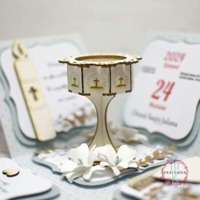 otwarte pudełko 3D, w środkowej jego części stoi chrzcielnica otoczona kwiatami białymi ręcznie wykonanymi