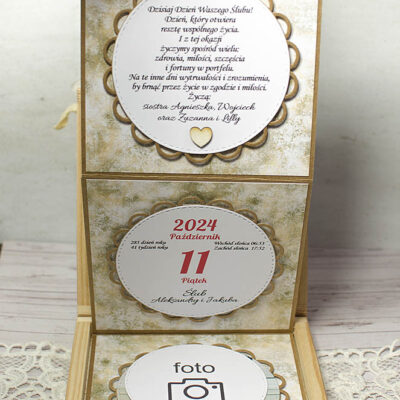 widok środka drewnianego pudełka po wyciągnięciu za wstążkę elementów ukazują się życzenia, kartka z kalendarza i zdjęcie pary młodej