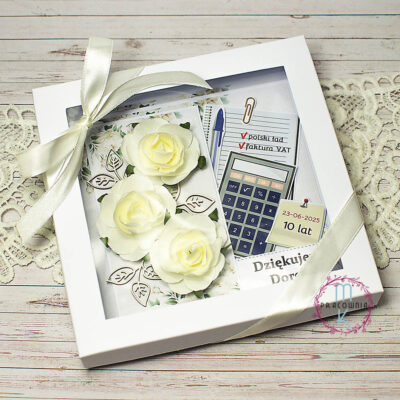 Po lewej stronie kartki znajdują się 3 kremowe przestrzenne róże otoczone listkami z tektury. Po prawej stronie są elementy nawiązujące do pracy księgowej i kadrowej: długopis, kalkulator, karteczka samoprzylepna, kartka zeszytowa na której można napisać np. faktura vat, polski ład albo coś innego czym dana osoba się zajmowała