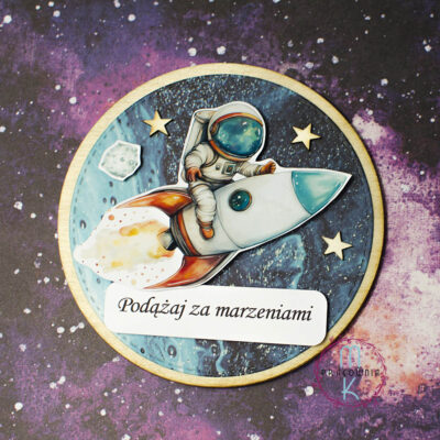 magnes okrągły na środku którego jest astronauta lecący na rakiecie. Pod rakietą napis Podążaj za marzeniami a w koło ozdobione jest gwiazdkami