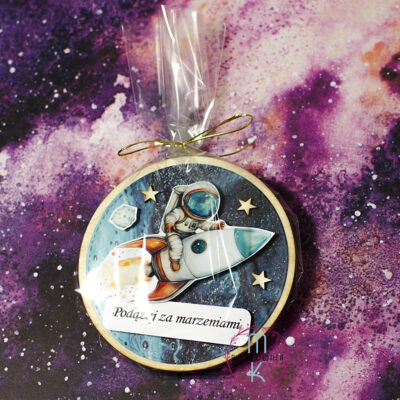 magnes okrągły na środku którego jest astronauta lecący na rakiecie. Pod rakietą napis Podążaj za marzeniami a w koło ozdobione jest gwiazdkami. Całość zapakowana w celofan
