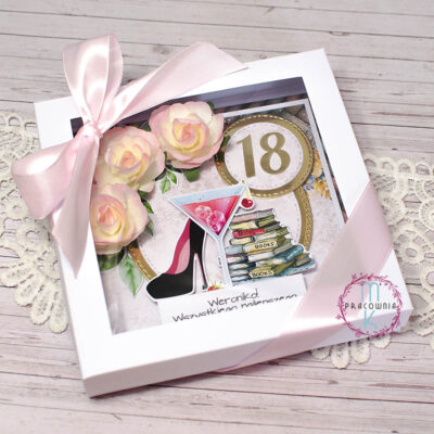 kartka zapakowana w pudełko białe z okienkiem i przewiązana jasno różową wstążką. W prawym górnym rogu cyfra 18, w lewym górnym rogu przestrzenne róże. Na środku kartki kieliszek z drinkiem, po jego lewej stronie but na wysokim obcasie a po prawej stronie od drinka jest stos książek. Pod spodem obrazków napis Weroniko wszystkiego najlepszego z okazji urodzin