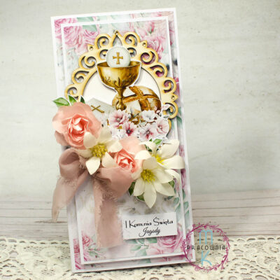 Kartka podłużna DL, w centralnym miejscu ozdobna tekturkowa ramka a w niej kielich, chleb i książeczka od nabożeństwa. Wokół lewej dolnej krawędzi ramki umieszczone kwiaty różowo białe a pod nimi wstążka pudrowy róż. Pod kwiatami napis Pierwsza Komunia Święta imię dziecka. Kartka w tonacji różowo białej