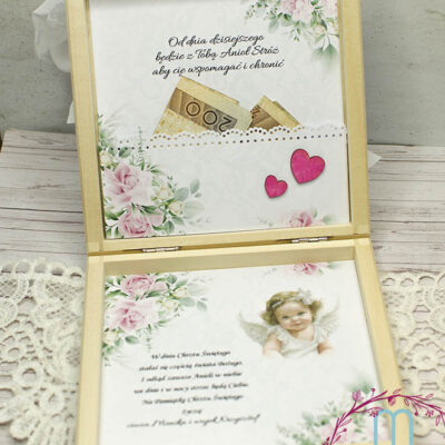 Środek drewnianego pudełka. Na górnej części jest cytat a pod spodem kieszonka na pieniądze. Kieszonka ozdobiona w dolnym prawym rogu różowymi serduszkami. Na dolnej części pudełka są życzenia z grafiką aniołka dziewczynki. Całość w tonacji białej z delikatnymi różowymi kwiatkami