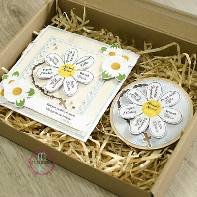 Zestaw prezentowy Apostolat Margaretka. W środku pudełka kartka z margaretką na której płatkach są imiona a w środku imię księdza. W zestawie również magnez z tą samą margaretką z imionami