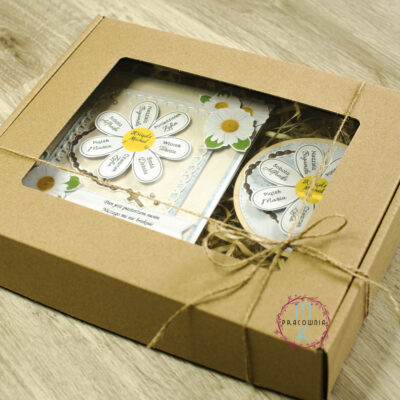 Zestaw prezentowy Apostolat Margaretka. W środku pudełka kartka z margaretką na której płatkach są imiona a w środku imię księdza. W zestawie również magnez z tą samą margaretką z imionami