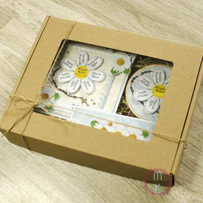 Zestaw prezentowy Apostolat Margaretka. W środku pudełka kartka z margaretką na której płatkach są imiona a w środku imię księdza. W zestawie również magnez z tą samą margaretką z imionami oraz zakładka do książki z cytatem