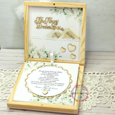 środek pudełka drewnianego. górnej części znajduje się napis Na nowej srodze życia i kieszonka na pieniądze. W dolnej części pudełka znajduje się kaskadowe kartki wyciągane za pomocą wstążki. Pierwsza kartka to życzenia