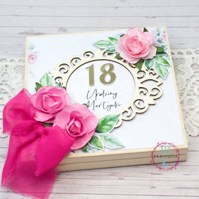 pamiatka w drewnianym pudełku z okazji 18 urodzin. W ozdobnej ramce umieszono cyfrę 18 i imię solenizantki. Wprawym górnym rogu znajduje się pojedyncza różowa róża i w dolnym lewym rogu znajdują się dwie róże z ozdobną wstążką w kolorze różowym