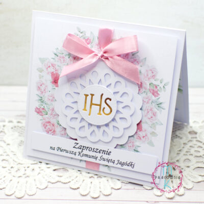 W centralnej części zaproszenia jest wianek z różowych kwiatów a wewnątrz niego jest złoty napis IHS. Całość przewiązana jest różową wstążką u góry zaproszenia